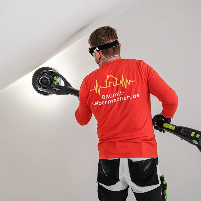 Der Heimwerker schleift die Wand mit einem Trockenbauschleifer.