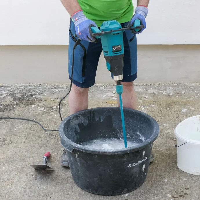 Heimwerker mischt den Münchner Rauputz mit Wasser und elektrischem Rührgerät im Mörtelkübel.