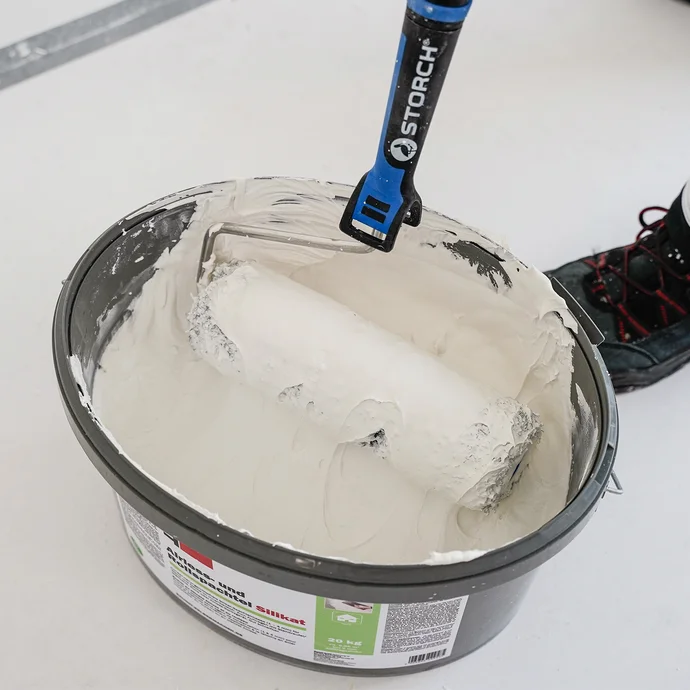 Farbeimer mit wei&szlig;er Wandfarbe und Farbrolle f&uuml;r Heimwerkerprojekte im Innenausbau.