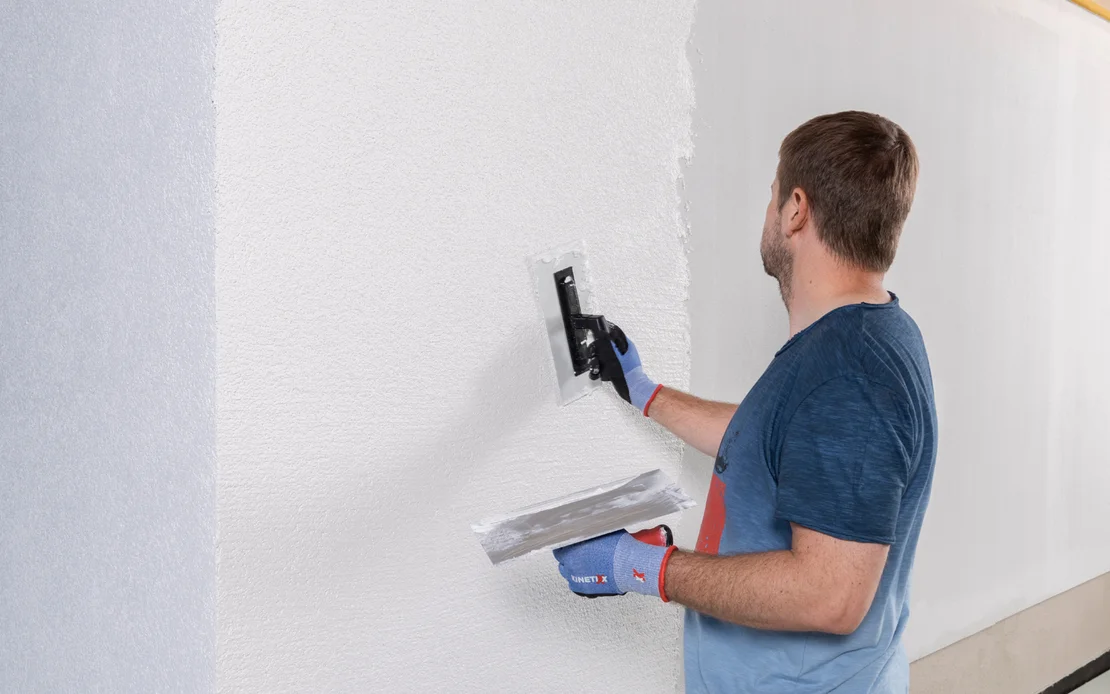 Mann tr&auml;gt mit Spachtel Putz auf Innenwand auf, Schritt-f&uuml;r-Schritt-Anleitung zur Wandrenovierung mit Baumit-Produkten.