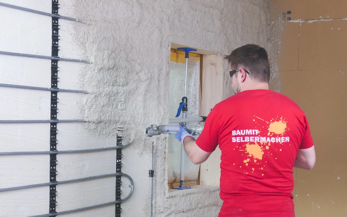 Putz wird von Heimwerker mit Putzmaschine auf eine Wand mit einer wassergef&uuml;hrten Wandheizung (Heizschlangen) aufgetragen.