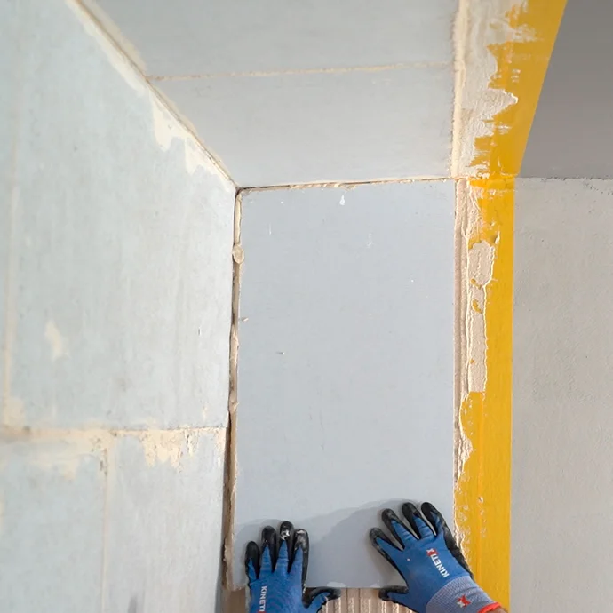 Heimwerker setzt den Kalziumsilikatplatte Anschlusskeil vorsichtig in den frisch aufgetrgenen Putz. Der Keil st&ouml;&szlig;t b&uuml;ndig an die geklebte Platte an der Wand und Decke.