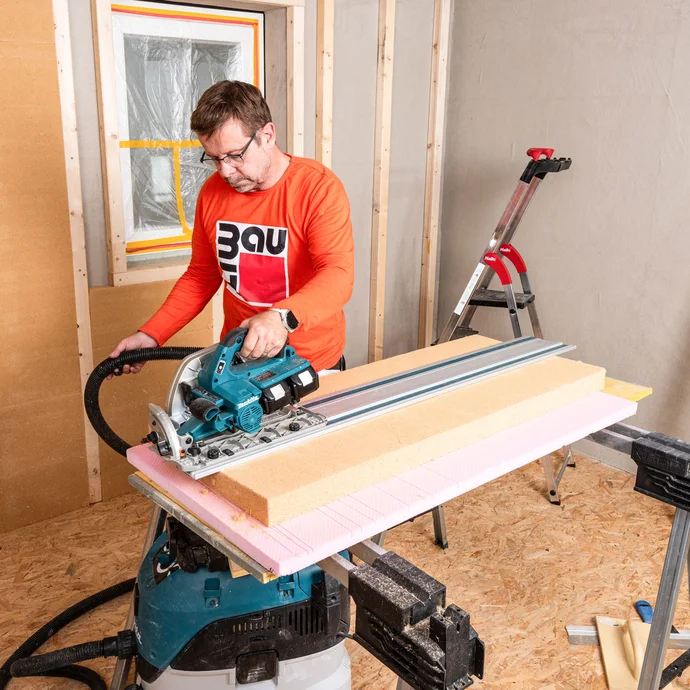 Heimwerker sägt die Holzfaserdämmplatte mit einer Handkreissäge und mit Hilfe einer Führungsschiene zu. So bekommst du exakte, gerade Schnittkanten der weichen Holzfaserdämmplatte.