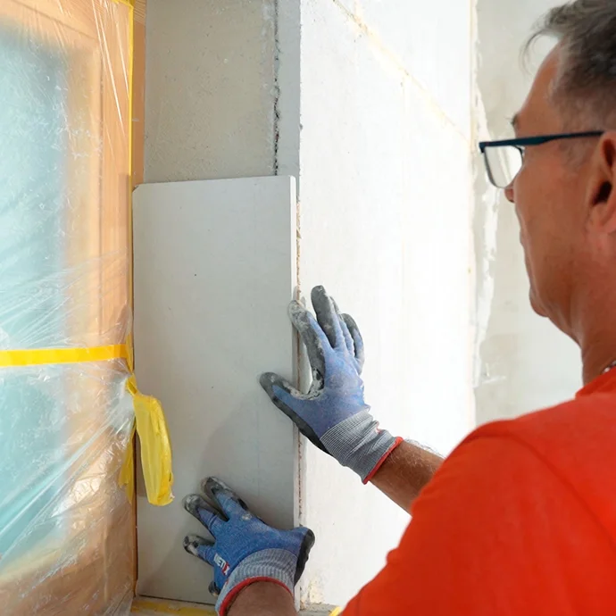 Heimwerker klebt die Kalziumsilikat Laibungsplatte in die seitliche Fensterlaibung.