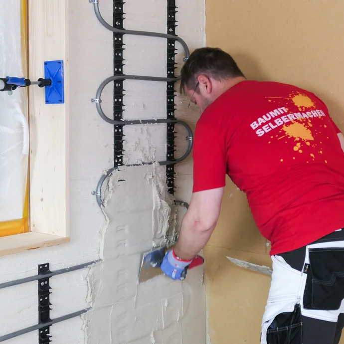 Heimwerker gl&auml;ttet den frisch aufgetragenen Putz &uuml;ber der Wandheizung mit einer Gl&auml;ttkelle.