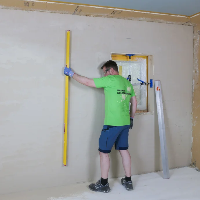 Die frisch verputzte Wand wird mit einer langen Wasserwaage gepr&uuml;ft, falls es noch unebene Stellen an der Wand gibt.