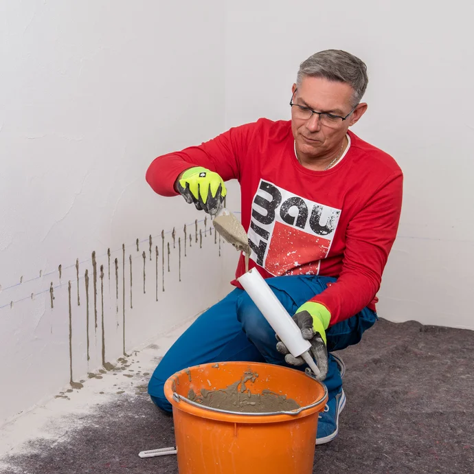 Handwerker f&uuml;llt Baumit Beton- und Reparaturspachtel in den Injektionstrichter.