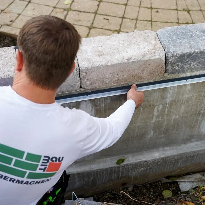 Handwerker drückt ein Abschlussprofil an die Wand und richtet es aus.