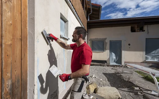 Heimwerker bettet das Gewebe flächig mit der glatten Seite der Zahnkelle in den Armierungsmörtel an der Fassade ein.
