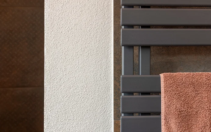Detailfoto van een moderne badkamer: verschillende donkere, roestkleurige platen en een handdoekhouder komen perfect tot hun recht tegen stralend witte muren met een fijne, gevilte structuur van Baumit-afwerkpleister InStyle Edelwit.