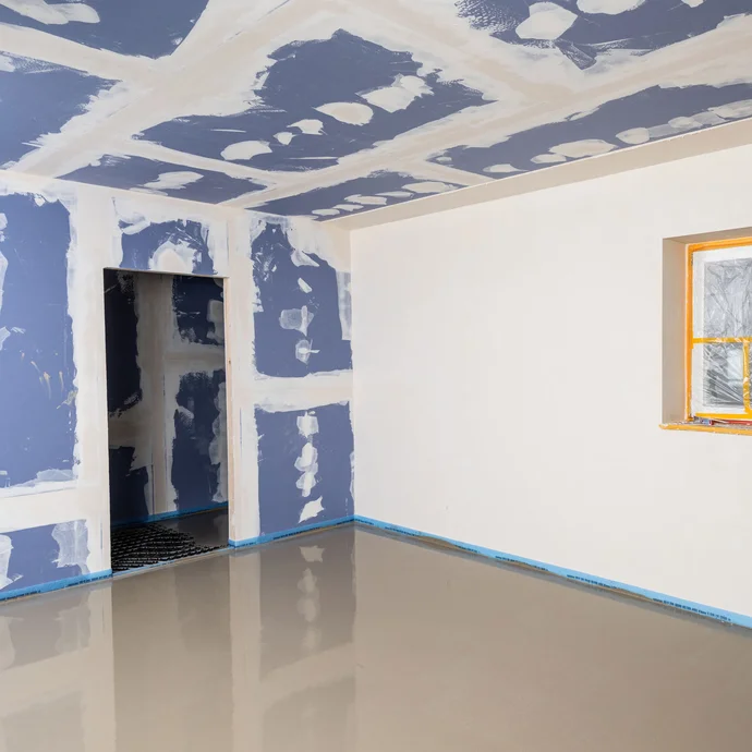 Raum mit frisch eingebauter Ausgleichsmasse.  Trockenbauwände mit Rigipsplatten und verputzte Wand mit abgeklebtem Fenster.