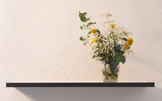 Muren met de afwerkpleister InStyle Edelwit voor een gezond woonklimaat, uitgevoerd in een fijne, gevilte structuur en gedecoreerd met een wandplank en een boeket bloemen.