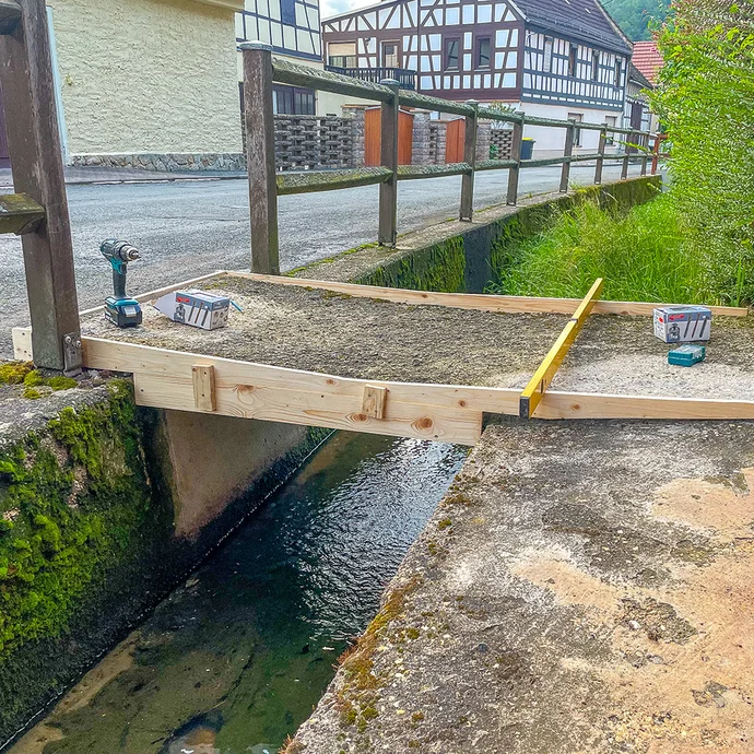 Holzschalung wird über dem Graben montiert und mit Schrauben fixiert, die Ausrichtung wird mit der Wasserwaage kontrolliert.