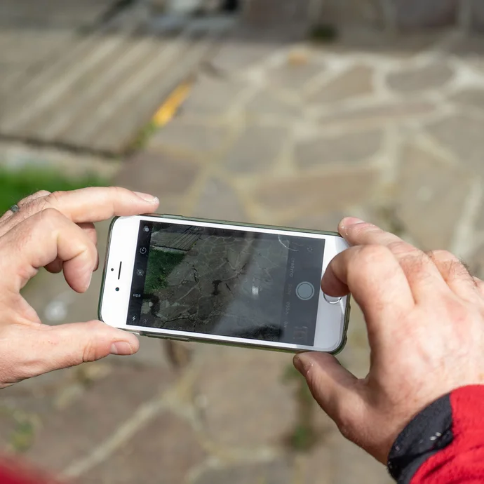 Person fotografiert mit dem Smartphone eine Pflasterfläche zur Dokumentation der Plattenpositionen.