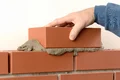 Heimwerker mauert Ziegelsteinwand mit Mörtel; Hand fügt oberen Ziegel hinzu für stabile Bauweise.