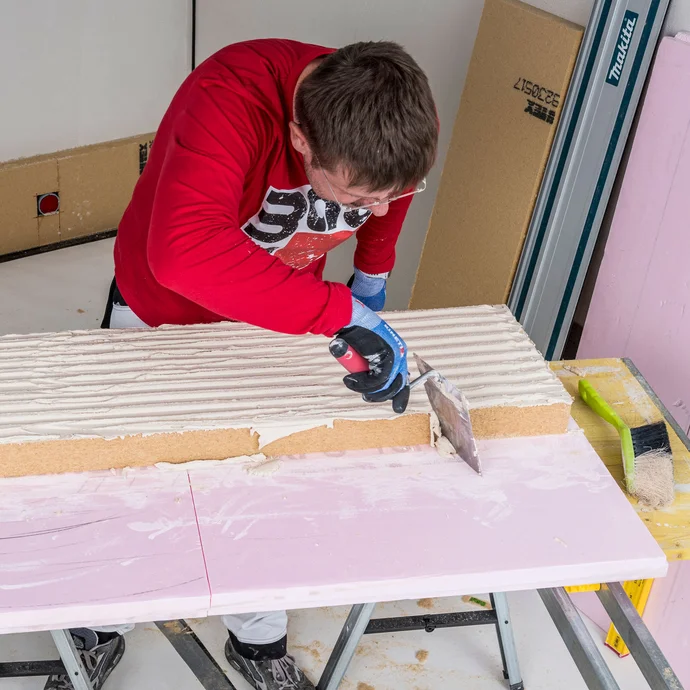 Heimwerker streift &uuml;berstehenden Baumit Klebem&ouml;rtel mit einer Maurerkelle umlaufend von der Holzfaserd&auml;mmplatte ab &ndash; saubere Plattenkanten vor der Verklebung der Innend&auml;mmung sicherstellen, Baumit Selbermachen Anleitung.